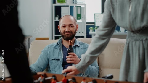 Wallpaper Mural Portrait of businessman holding bottle of beer after work at office. Person looking at colleagues playing football game at foosball table to have fun with activity. Man with drink Torontodigital.ca