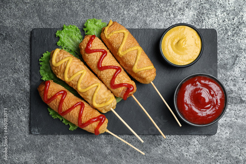 Canvas Print Delicious deep fried corn dogs with lettuce and sauces on grey table, top view