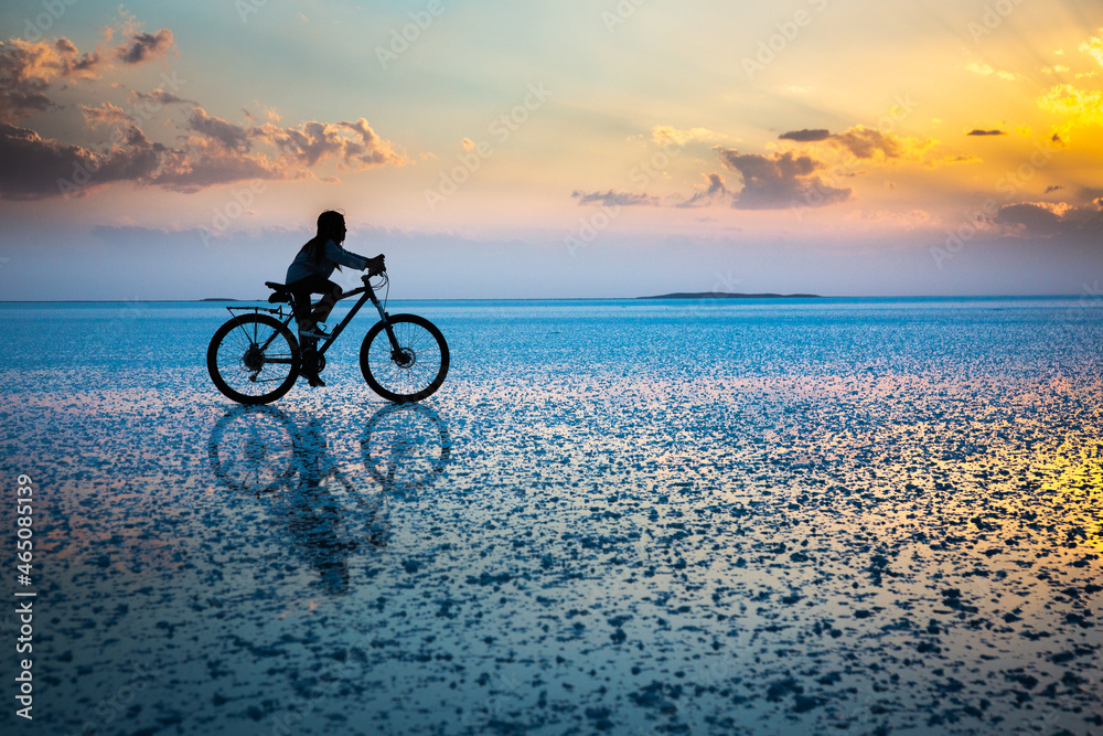 Fototapeta premium boy riding a bike over the reflection of a salt lake at sunset