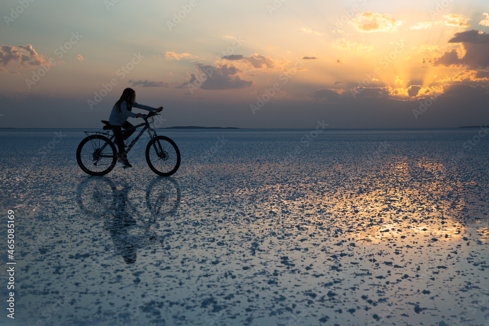 Fototapeta premium boy riding a bike over the reflection of a salt lake at sunset