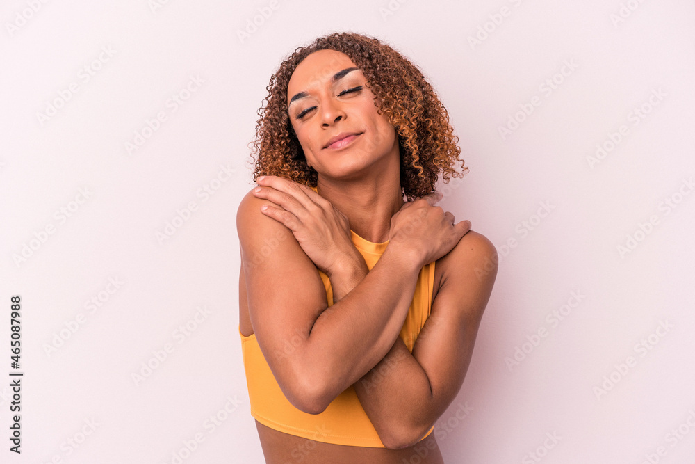 Young latin transsexual woman isolated on pink background hugs, smiling carefree and happy. - obrazy, fototapety, plakaty 