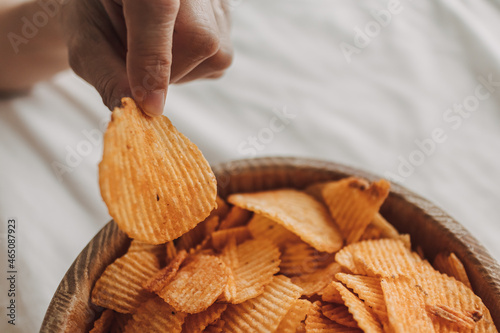 Bowl of potato chips on white sheet bed with hand picking up.