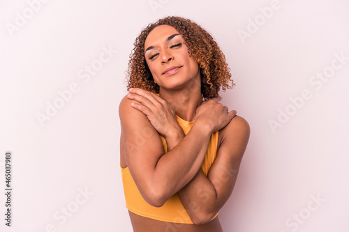 Young latin transsexual woman isolated on pink background hugs, smiling carefree and happy.