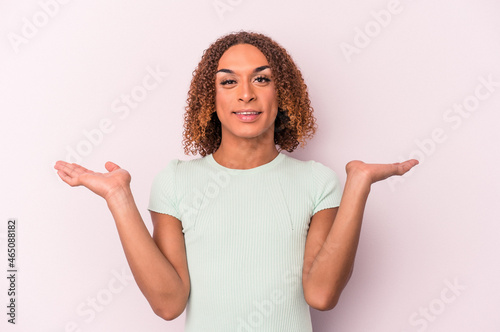 Young latin transsexual woman isolated on pink background makes scale with arms, feels happy and confident.