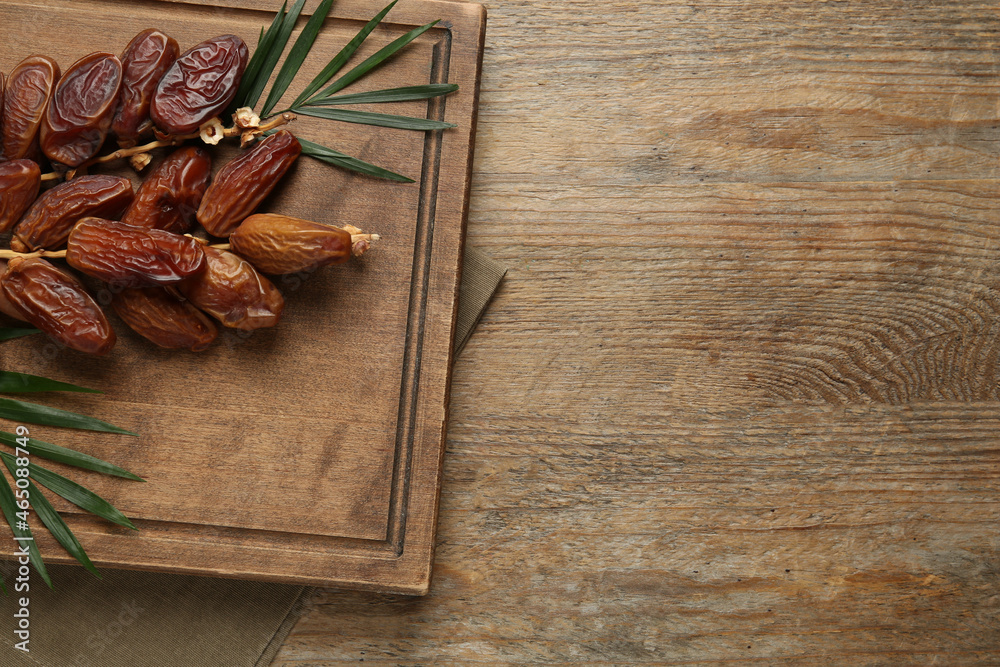 Sweet dried dates with green leaves on wooden table, top view. Space for text
