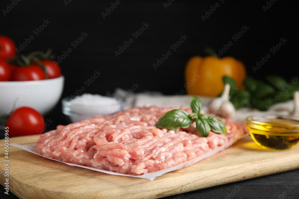 Raw chicken minced meat with basil on black wooden table, closeup