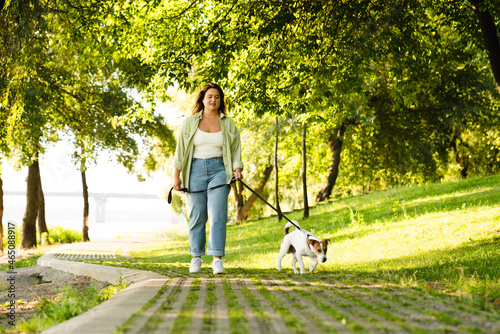 Young caucasian woman pet owner walking with her dog jack russell terrier in park outdoors. Pet care concept. Good boy