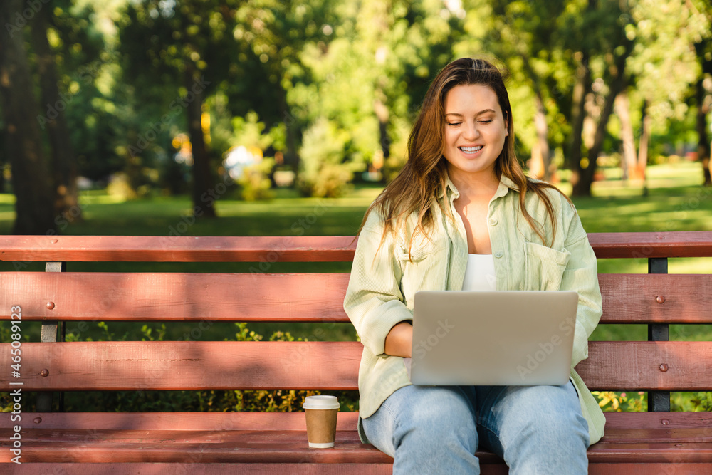 Young freelancer woman student working e-learning on distance remotely on laptop, watching webinars, doing homework, preparing project for deadline sitting on park bench Young freelancer woman student working e-learning on distance remotely on laptop, watching webinars, doing homework, preparing project for deadline sitting on park bench