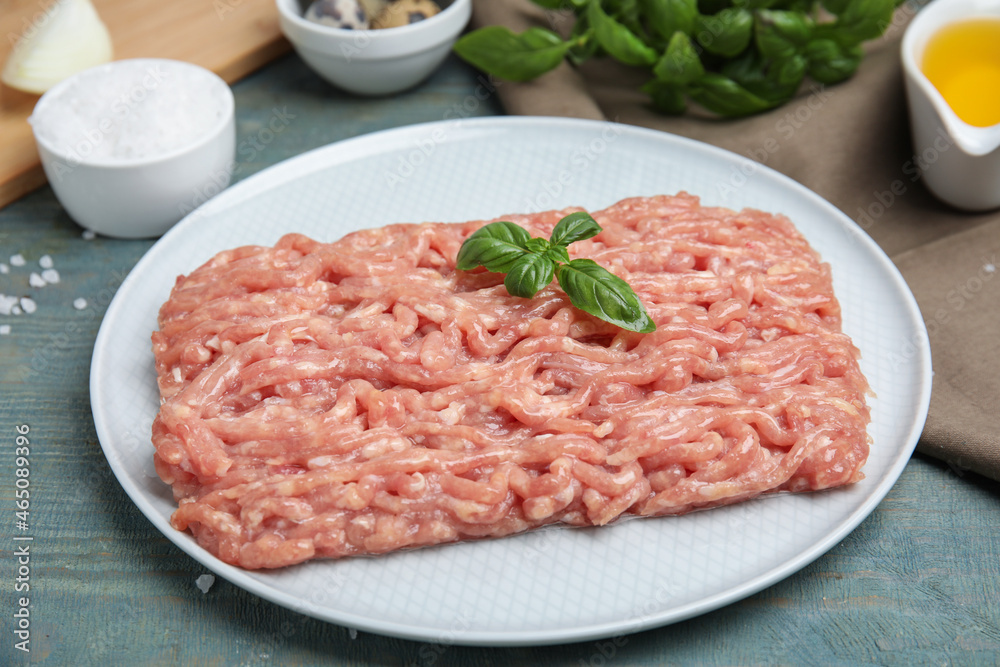 Raw chicken minced meat with basil on light blue wooden table, closeup