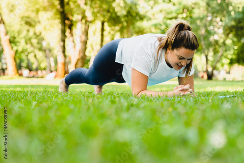 Fit strong slimming caucasian woman athlete standing in plank position, losing weight on fitness yoga training class on the grass lawn in park outdoors