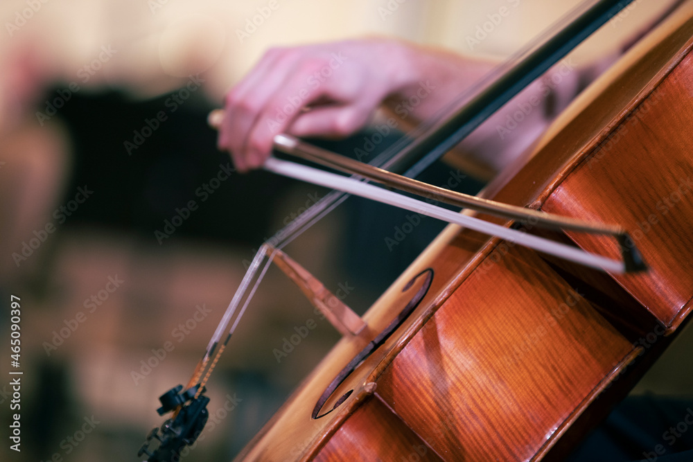 A musicians hand holding a bow and playing a cello during a rehearsal or a concert of a symphony orchestra A musicians hand holding a bow and playing a cello during a rehearsal or a concert of a symphony orchestra