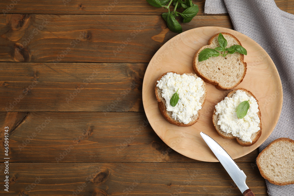 Bread with cottage cheese and basil on wooden table, flat lay. Space for text