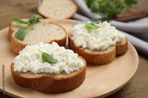 Bread with cottage cheese and basil on wooden table, closeup