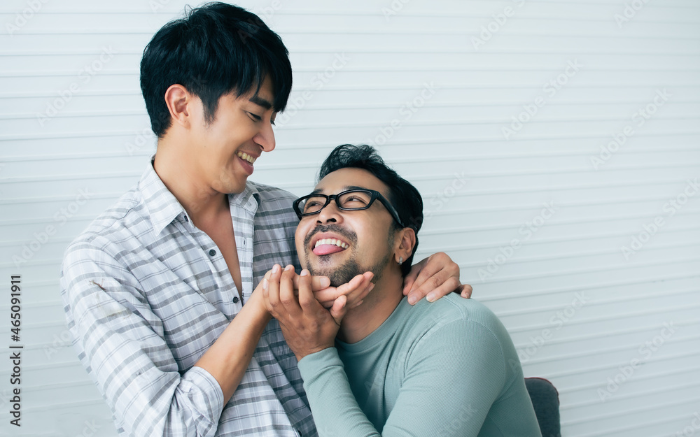 Portrait Gay LGBT sweet Asian couple wearing pajamas, smiling and hugging with happiness and love, sitting in living room at home with comfortable, cute posing in Lifestyle Concept with copy space. Portrait Gay LGBT sweet Asian couple wearing pajamas, smiling and hugging with happiness and love, sitting in living room at home with comfortable, cute posing in Lifestyle Concept with copy space.