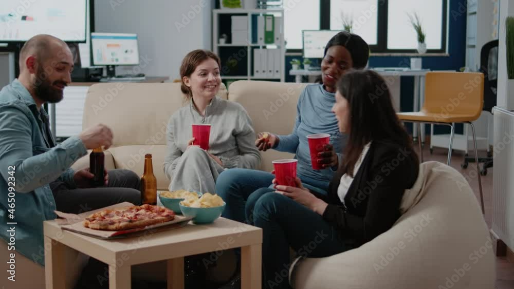 Multi ethnic group of people enjoying beer and pizza to have fun with activity after work. Cheerful workmates drinking alcohol from cups and bottles while talking. Entertainment at office. Multi ethnic group of people enjoying beer and pizza to have fun with activity after work. Cheerful workmates drinking alcohol from cups and bottles while talking. Entertainment at office.