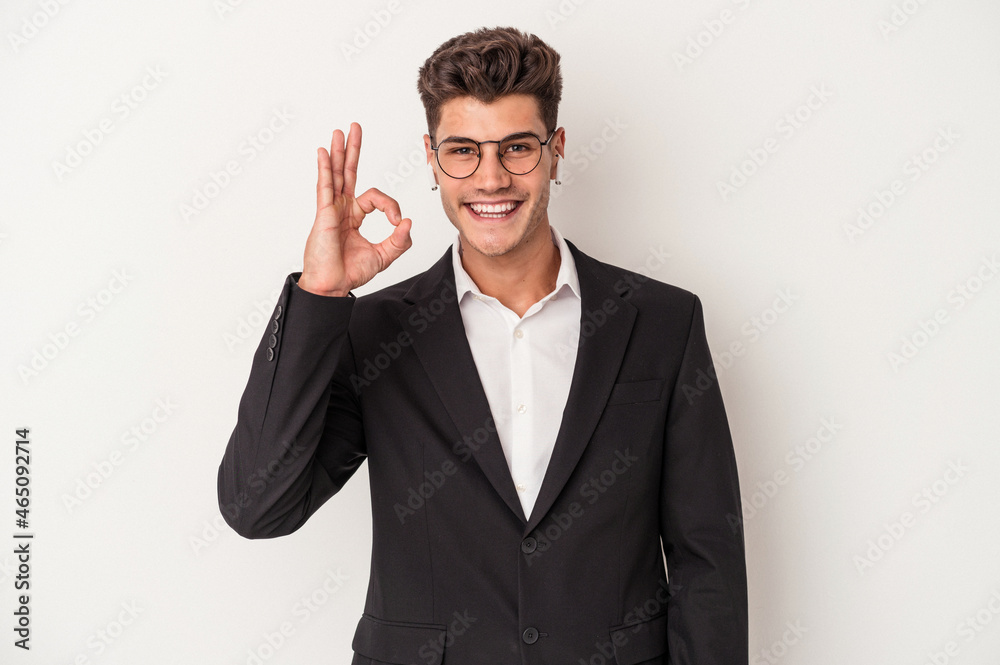 Young business caucasian man wearing headphones isolated on white background cheerful and confident showing ok gesture. Young business caucasian man wearing headphones isolated on white background cheerful and confident showing ok gesture.
