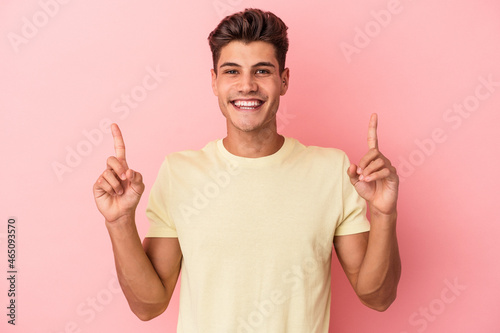 Young caucasian man isolated on pink background indicates with both fore fingers up showing a blank space.