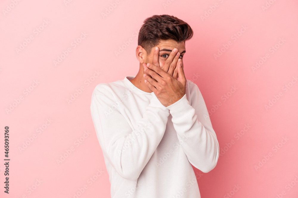Young caucasian man isolated on pink background blink through fingers frightened and nervous. Young caucasian man isolated on pink background blink through fingers frightened and nervous.