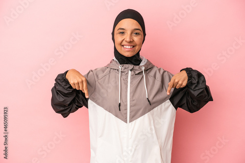 Young Arab woman with sport burqa isolated on pink background points down with fingers, positive feeling.