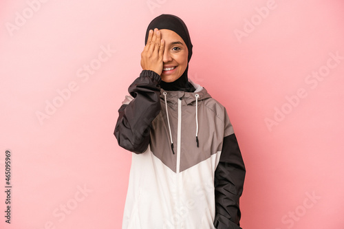 Young Arab woman with sport burqa isolated on pink background having fun covering half of face with palm.