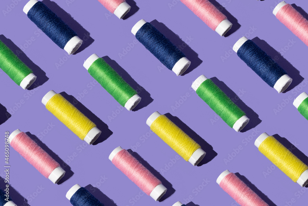 sewing thread in pink yellow, green and blue color . minimal pattern concept on purple background. sewing thread in pink yellow, green and blue color . minimal pattern concept on purple background.