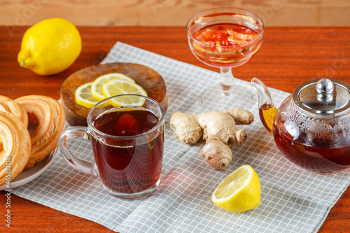 A teapot ofstrong tea and a cup on the table next to ginger lemon, donuts with cream on a napkin. photo