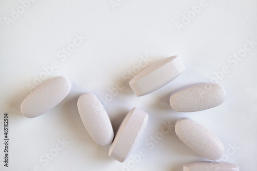 White or light grey long vitamins or pills on white background, macro, close-up, copy space, flatly. Nutritional supplements concept, health, vitamins, monochrome minimal style. Horizontal