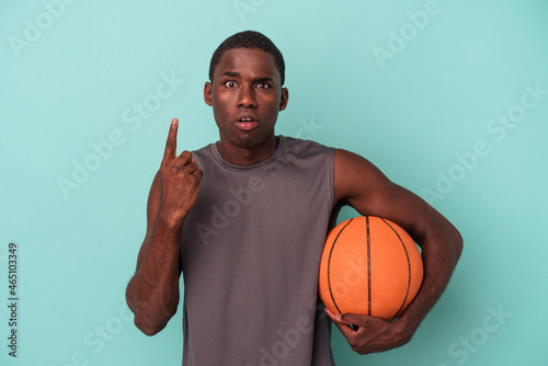 Young African American man playing basketball isolated on blue background having some great idea, concept of creativity. © Asier