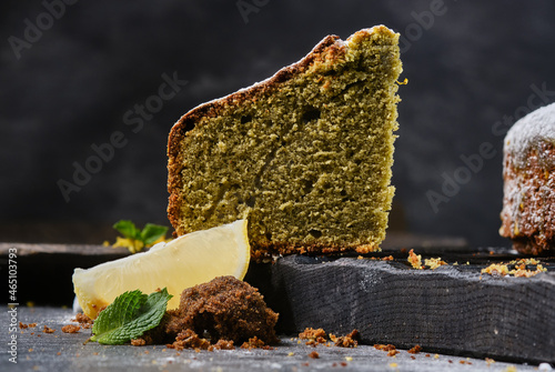 Piece of bundt cake or muffin cake from lemon and mint decorated icing sugar on a black wooden cutting board. Sieving powdered sugar on a Christmas cake.  photo