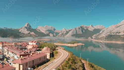 aerial drone shot of a swamp located in the town of Riaño, a village with a road with a bridge that divides the lake on a sunny day with the stone mountains in the background