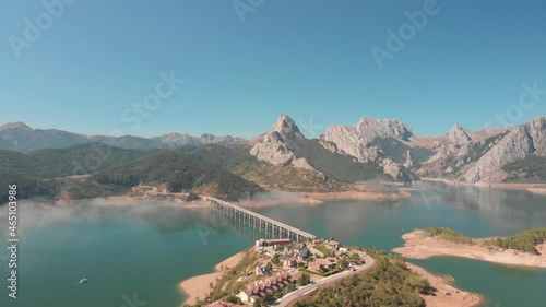 aerial drone shot of a swamp located in the town of Riaño, a village with a road with a bridge that divides the lake on a sunny day with the stone mountains in the background