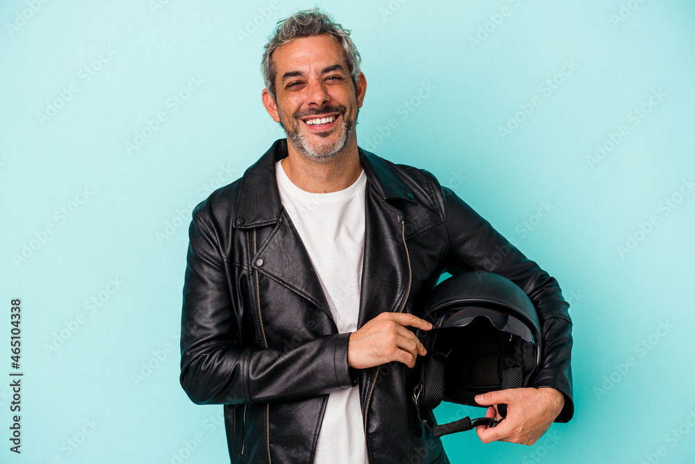 Middle age biker caucasian man holding helmet isolated on blue background laughing and having fun. Middle age biker caucasian man holding helmet isolated on blue background laughing and having fun.