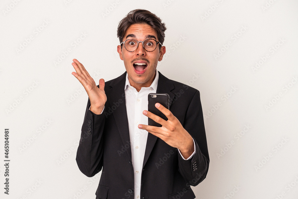 Young mixed race business man holding mobile phone isolated on white background surprised and shocked. Young mixed race business man holding mobile phone isolated on white background surprised and shocked.