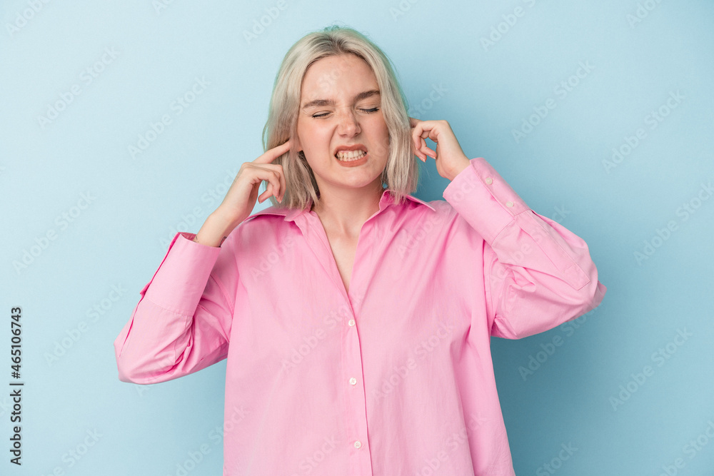 Young caucasian woman isolated on blue background covering ears with fingers, stressed and desperate by a loudly ambient. Young caucasian woman isolated on blue background covering ears with fingers, stressed and desperate by a loudly ambient.