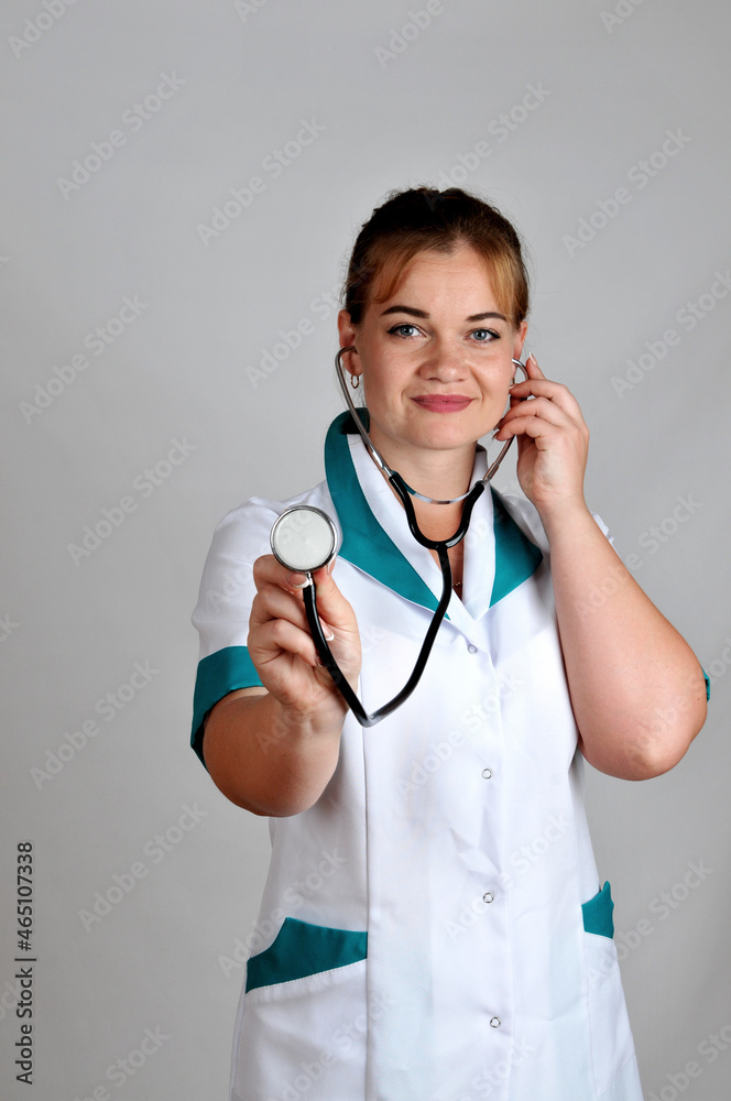 Female doctor in a uniform holding a stethoscope against a grey background Female doctor in a uniform holding a stethoscope against a grey background