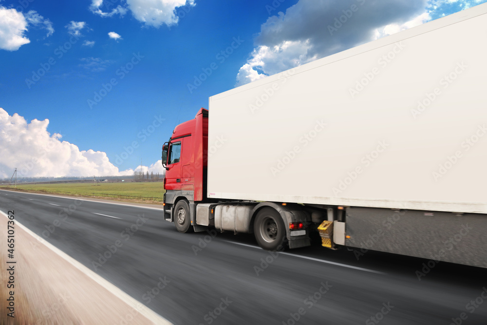 Truck with a white trailer with blank space for text on a road in motion against a sky with clouds Truck with a white trailer with blank space for text on a road in motion against a sky with clouds
