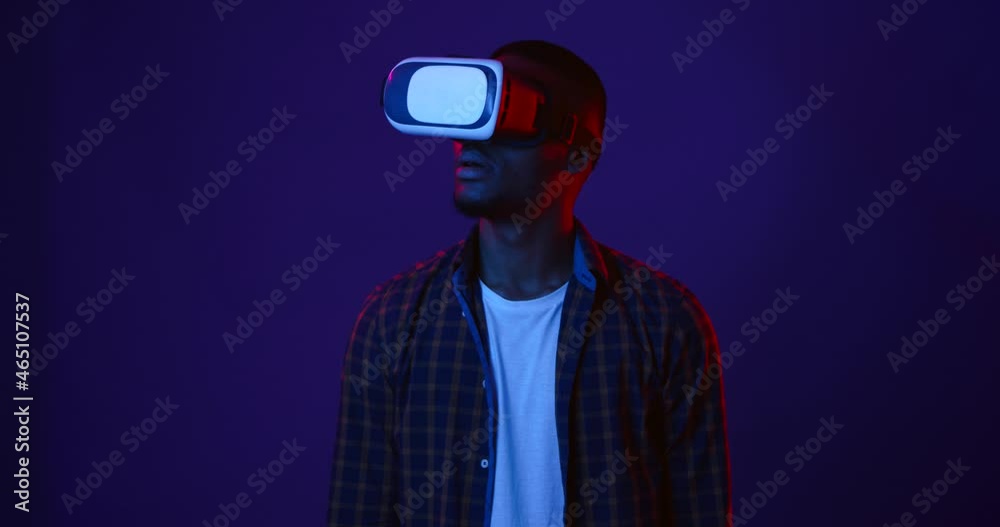 Futuristic technologies. African american man wearing virtual reality glasses watching video, neon lights background