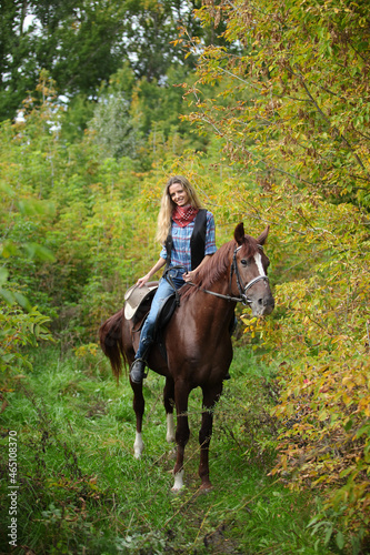 Beautiful cowgirl ride her horse in autumn country road at sunset