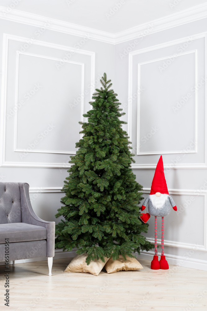 Fototapeta premium Christmas tree close-up without toys. Red toy elf gnome near the Christmas tree. Good New Year spirit.