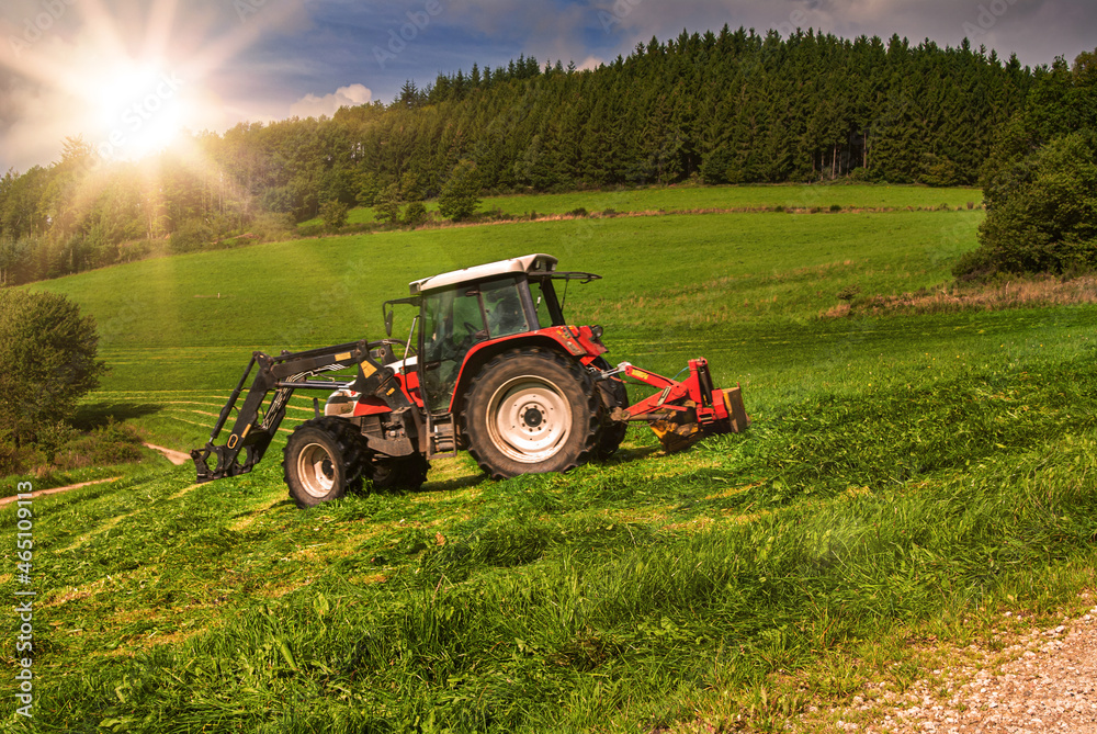 Traktor mit Mähwerk beim mähen einer Wiese bei Gegenlicht im Sauerland Traktor mit Mähwerk beim mähen einer Wiese bei Gegenlicht im Sauerland