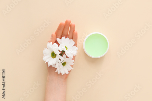 Woman with hand cream and flowers on light background