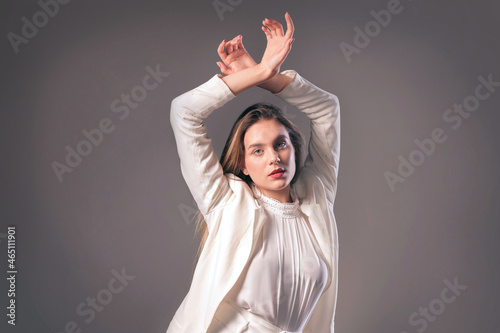 Young beautiful gentle woman wearing  white suit dancing and posing over grey wall. Calm mood. Hands up. Beauty People Emotions Fashion Lifestyle Mysterious Dance concept. Blurred details.