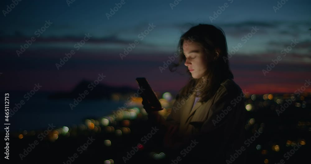 Cinematic dusk shot in dark setting of young woman look at phone and scroll through different pages and apps. Student or freelancer use technology for online shopping or job search
