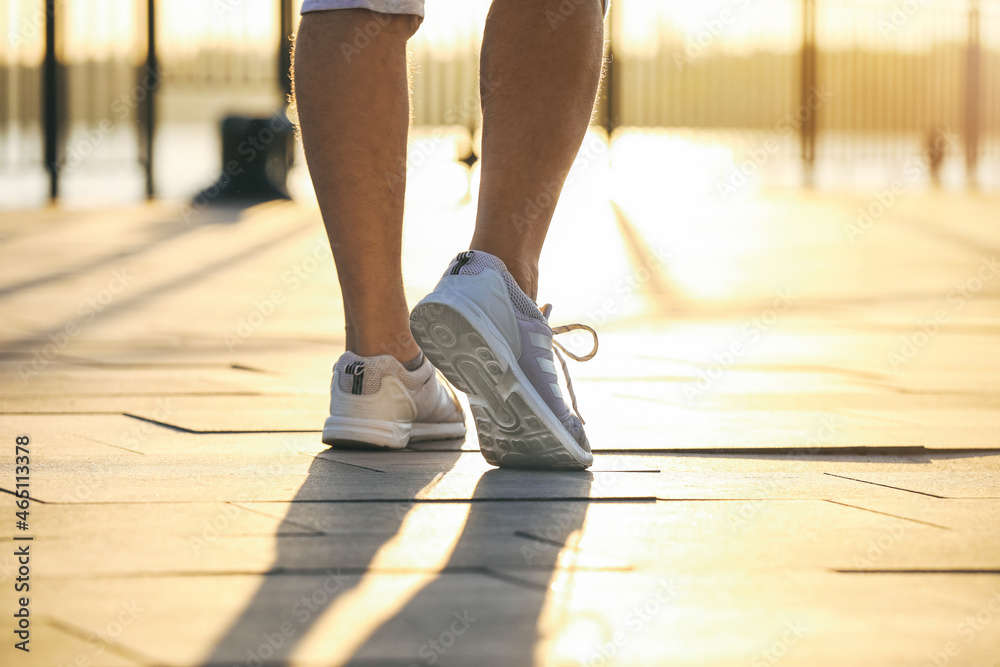 Legs of sporty young man walking at sunset, closeup