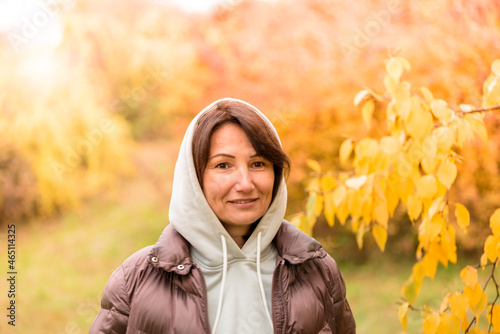 Portrait of a cute woman in a hoodie outdoors on the background of an autumn park