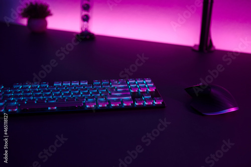 Low light scene of computer input devices, pink illuminated wall in background.