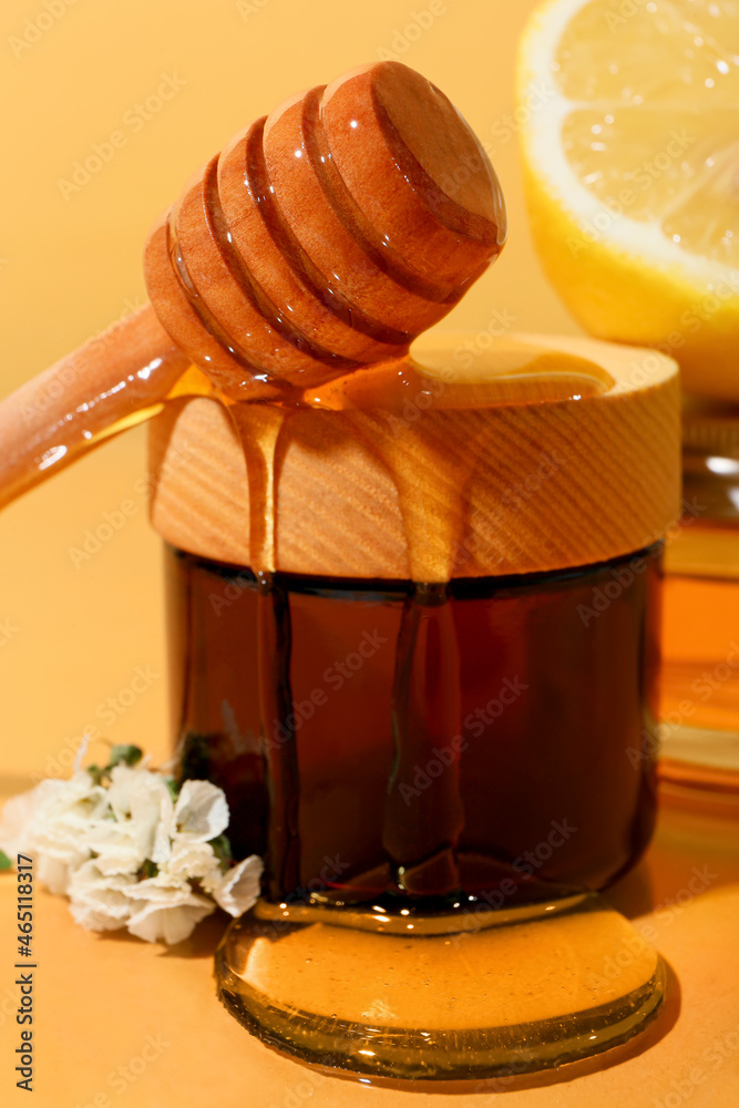 Pouring of honey from dipper onto jar with cosmetic product on color background, closeup Pouring of honey from dipper onto jar with cosmetic product on color background, closeup