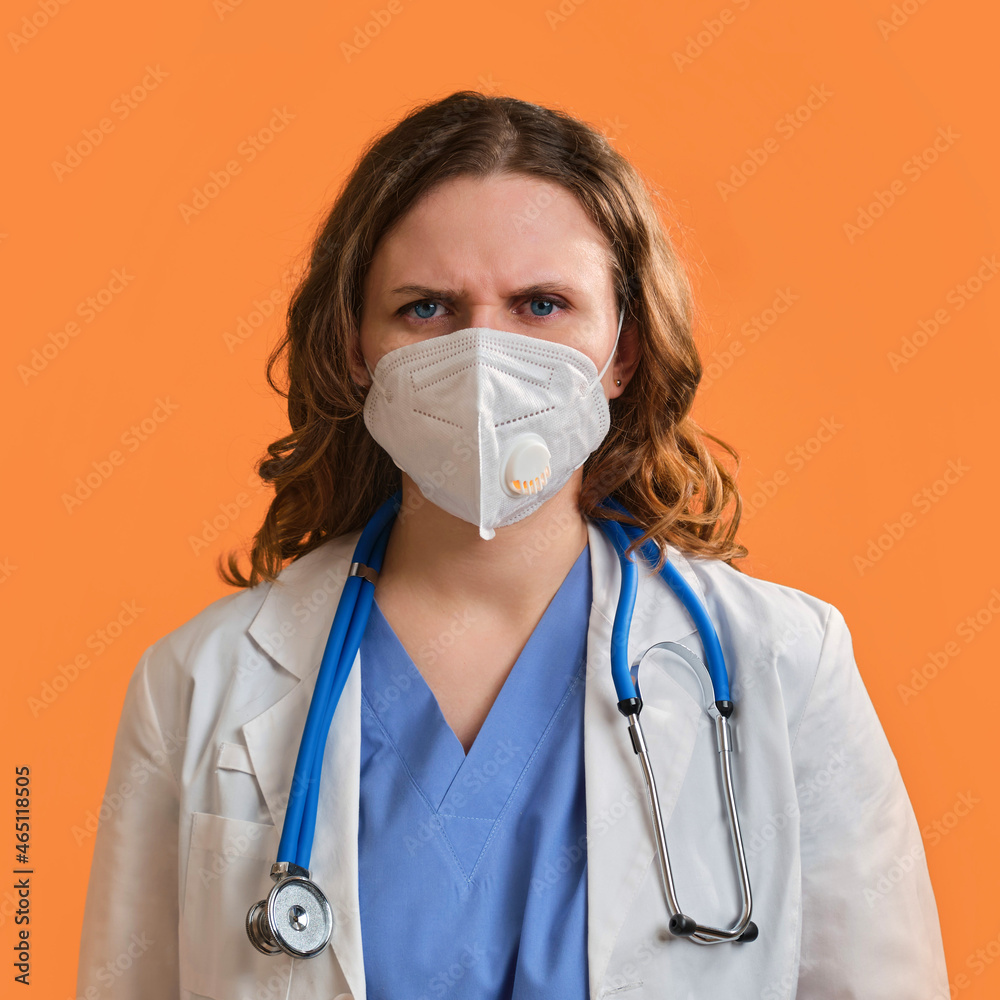 Portrait of a doctor woman with angry facial expression, close up. Nurse in a blue uniform and a medical mask on a orange background Portrait of a doctor woman with angry facial expression, close up. Nurse in a blue uniform and a medical mask on a orange background