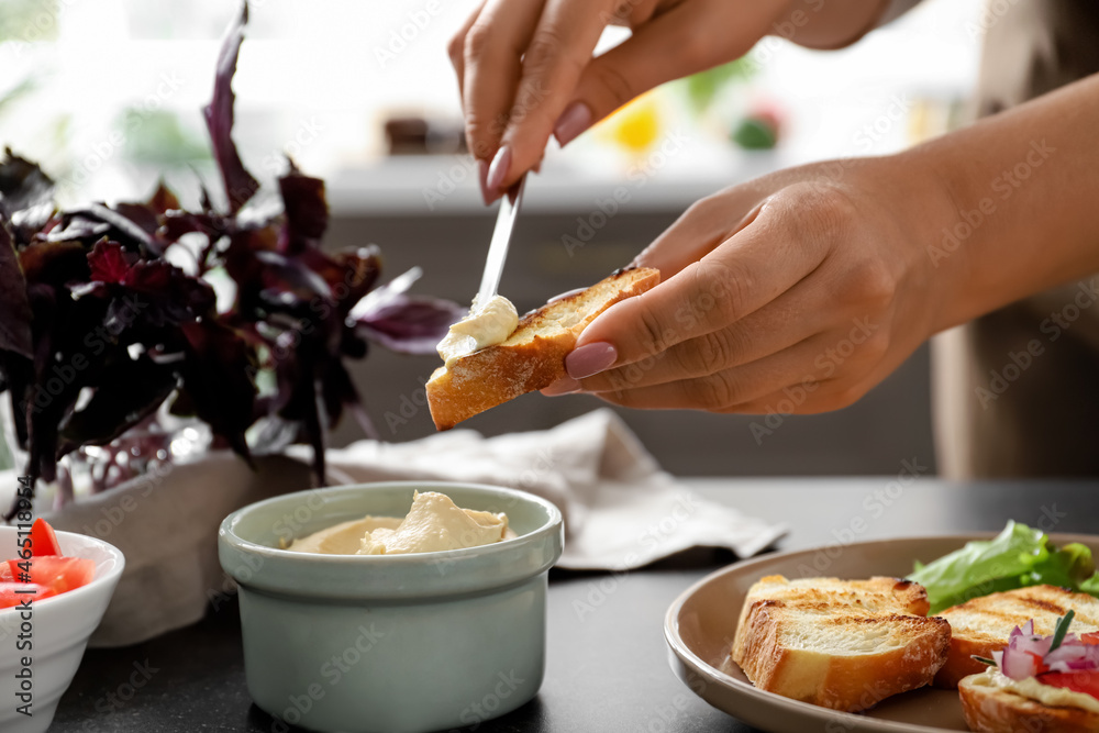 Woman spreading toast with dip at table in kitchen, closeup