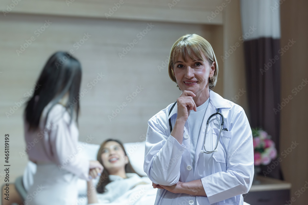 Fototapeta premium Caucasian senior woman doctor smiling while holding hand on chin and standing with background have the relatives visiting the patients who were treated improved.